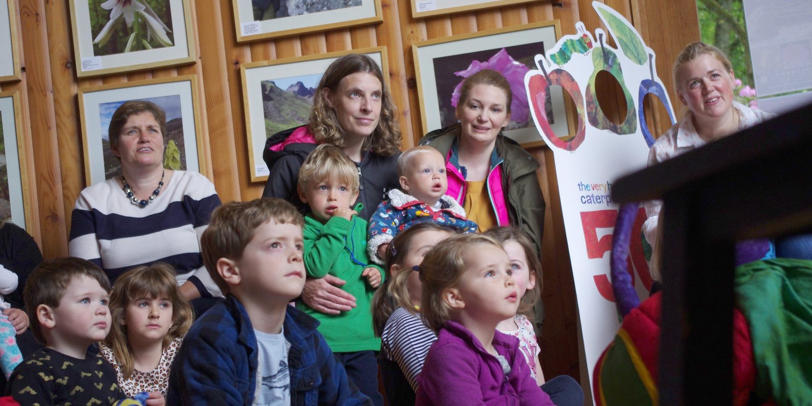 A photo of parents with children in a wooden room and looking in the same direction.