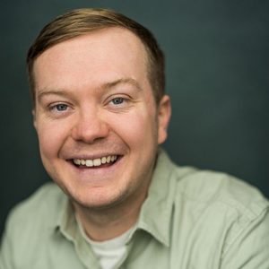 Smiling white man with short dark blonde hair. Wearing a shirt.