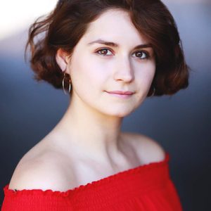 White woman with bobbed dark hair wearing a red top