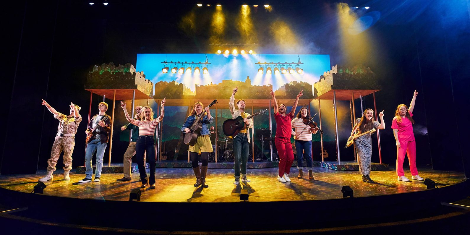 The cast of Sunshine on Leith at the front of the stage singing and playing instruments.
