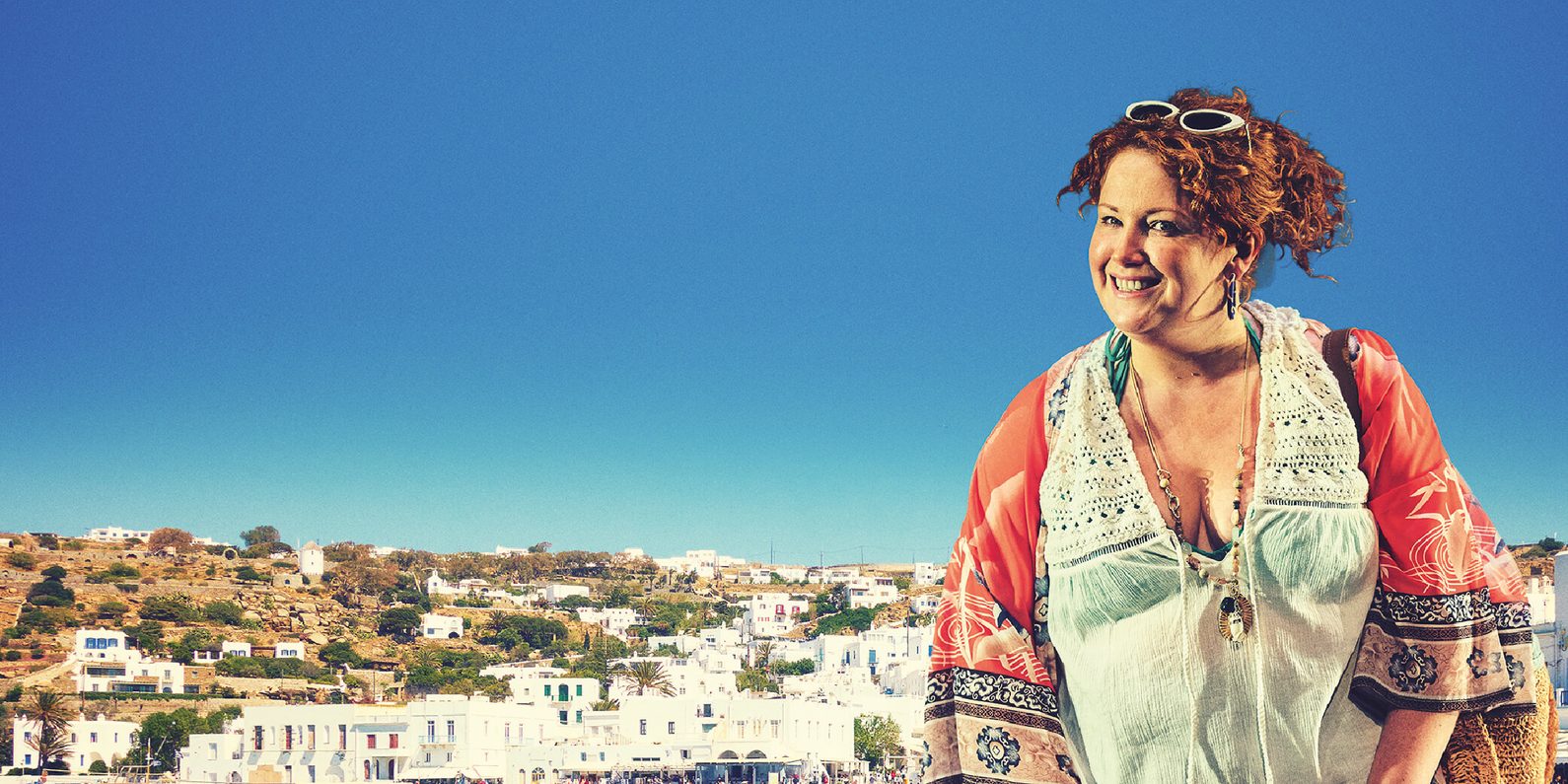 Smiling woman in summer holiday clothing standing in front of a mediterranean background.