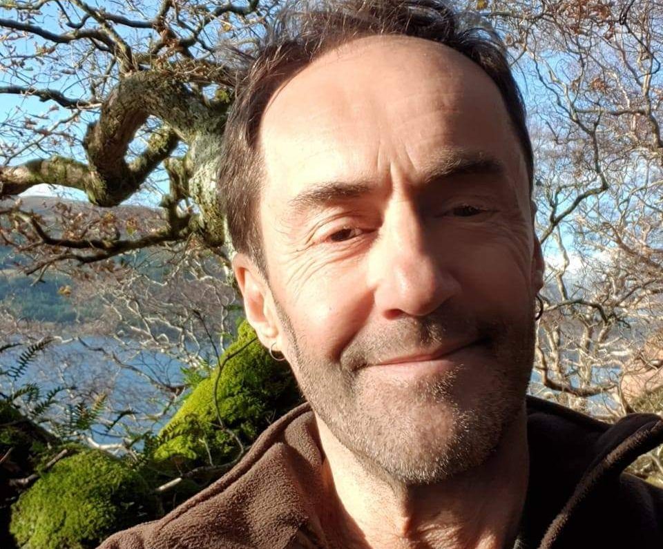 A man in a brown fleece with tree behind.