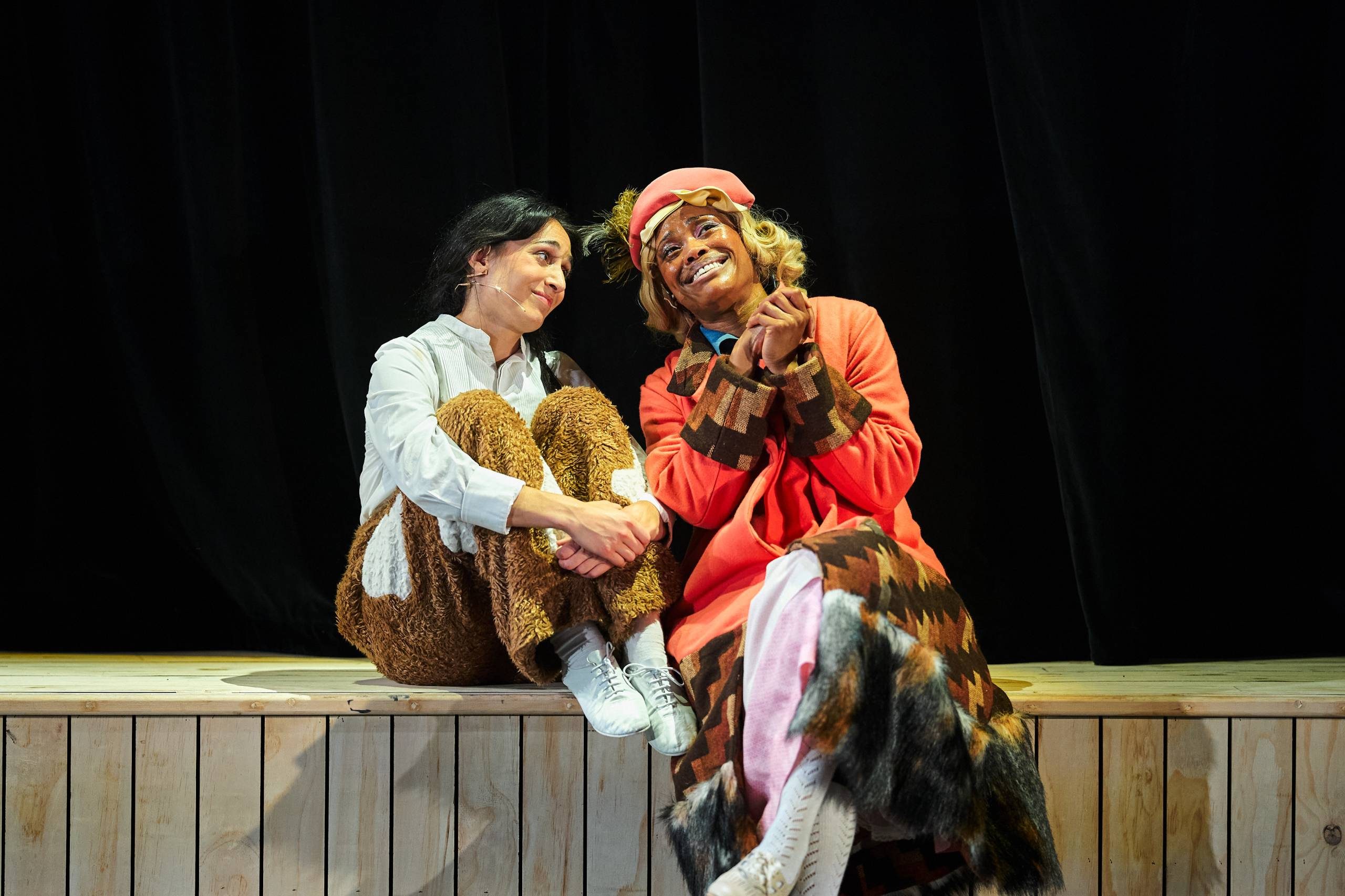 Two women sitting on a wall smiling.