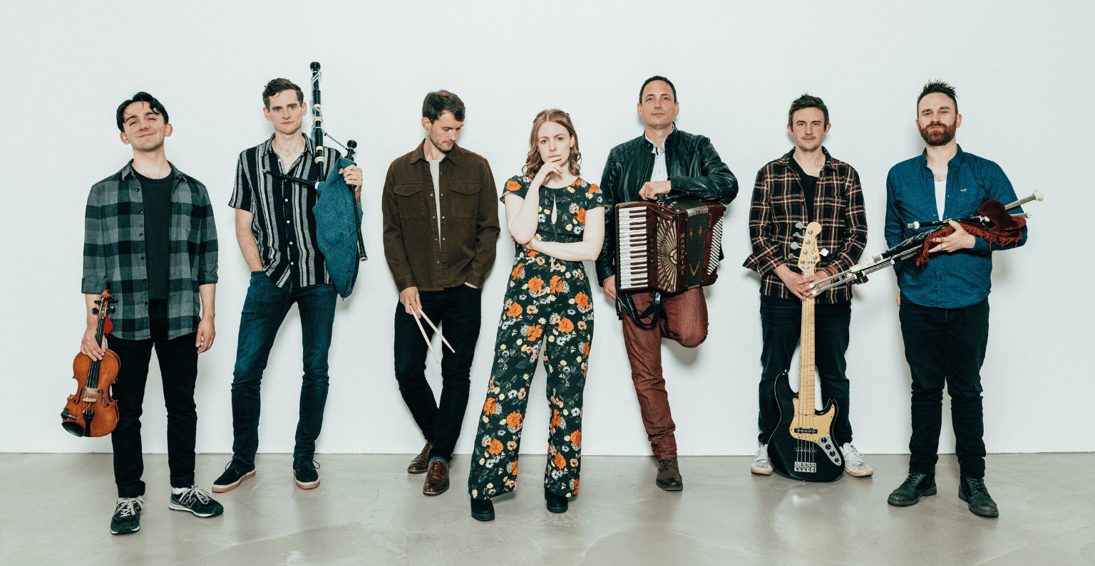Seven band members in front of a white wall holding instruments