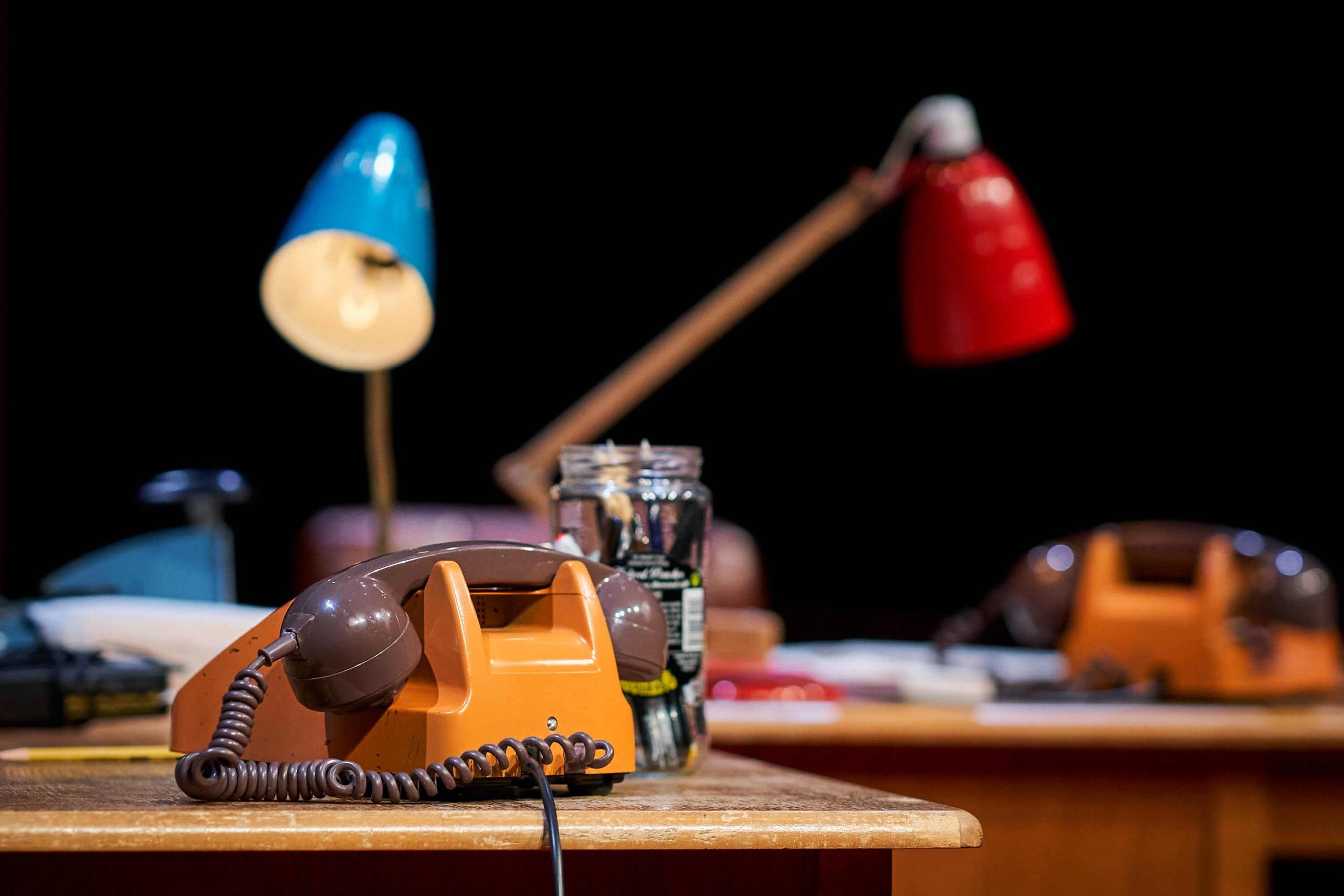 Two seventies telephones on desks with table lamps.