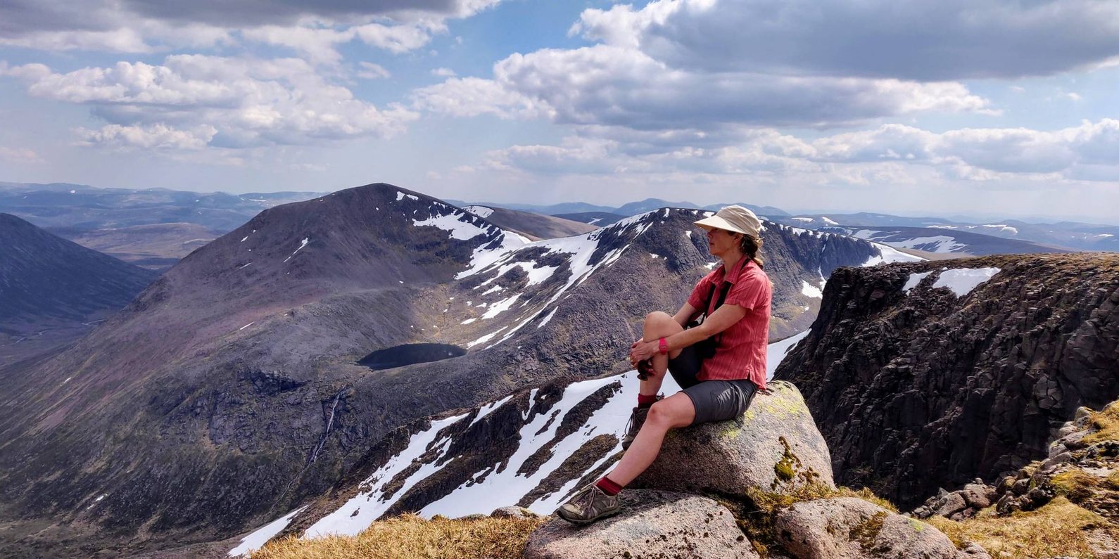 Woman witting on top of a mountain ridge with snow on the tops.