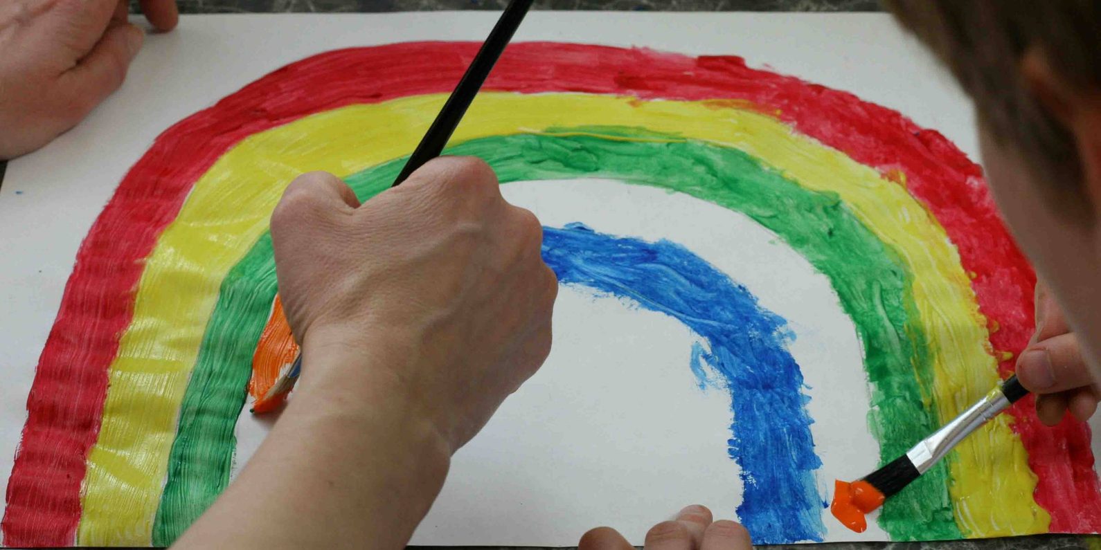 Hands painting a rainbow on a white sheet of paper