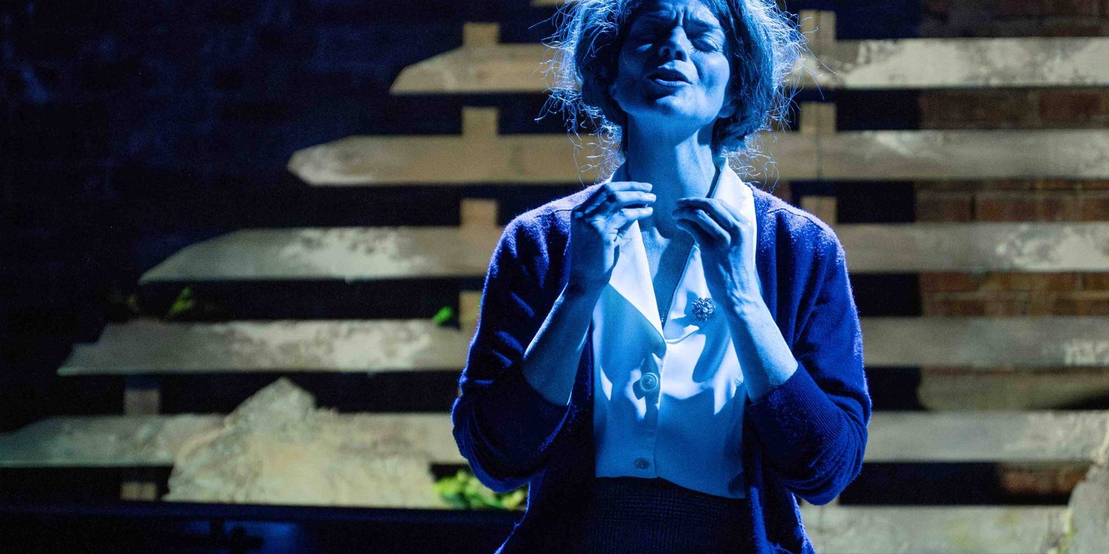 Actor on stage in mid performance. Eyes closed in blue tinted light.