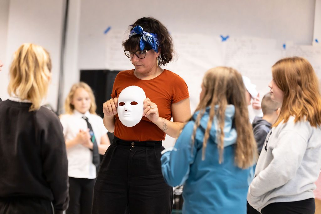 Woman holding a white mask in front of her with children watching