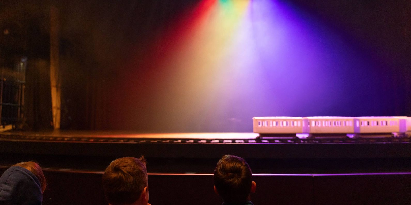 Children watching a model train on a stage. Different coloured lights illuminate the stage.