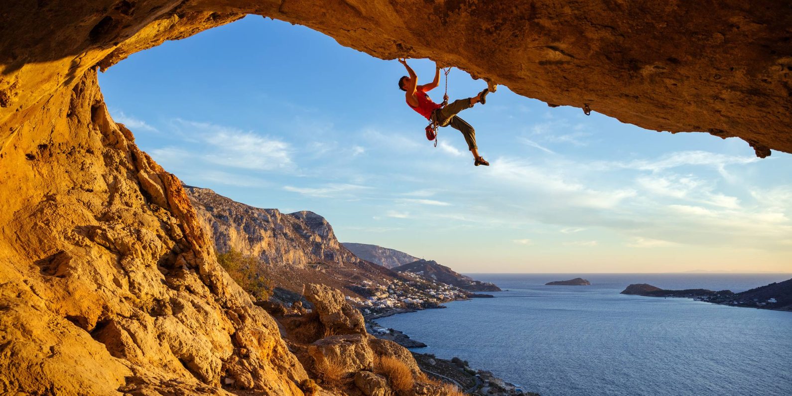 Male,Climber,On,Overhanging,Rock,Against,Beautiful,View,Of,Coast